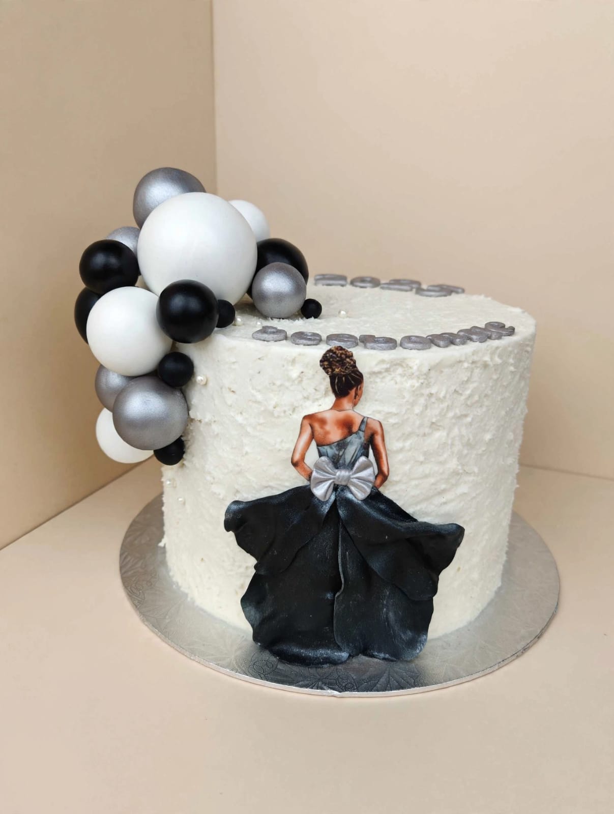 Textured white cake with a black gown silhouette and a monochrome balloon garland
