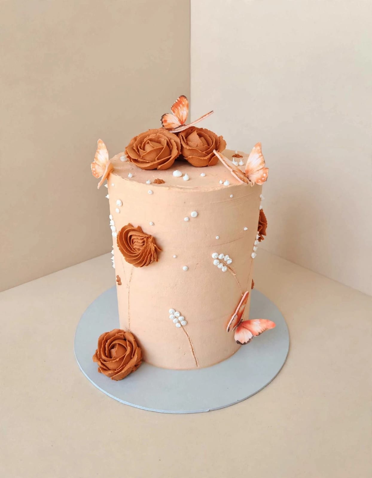 Tall caramel buttercream cake with piped roses, sugar pearls and butterflies