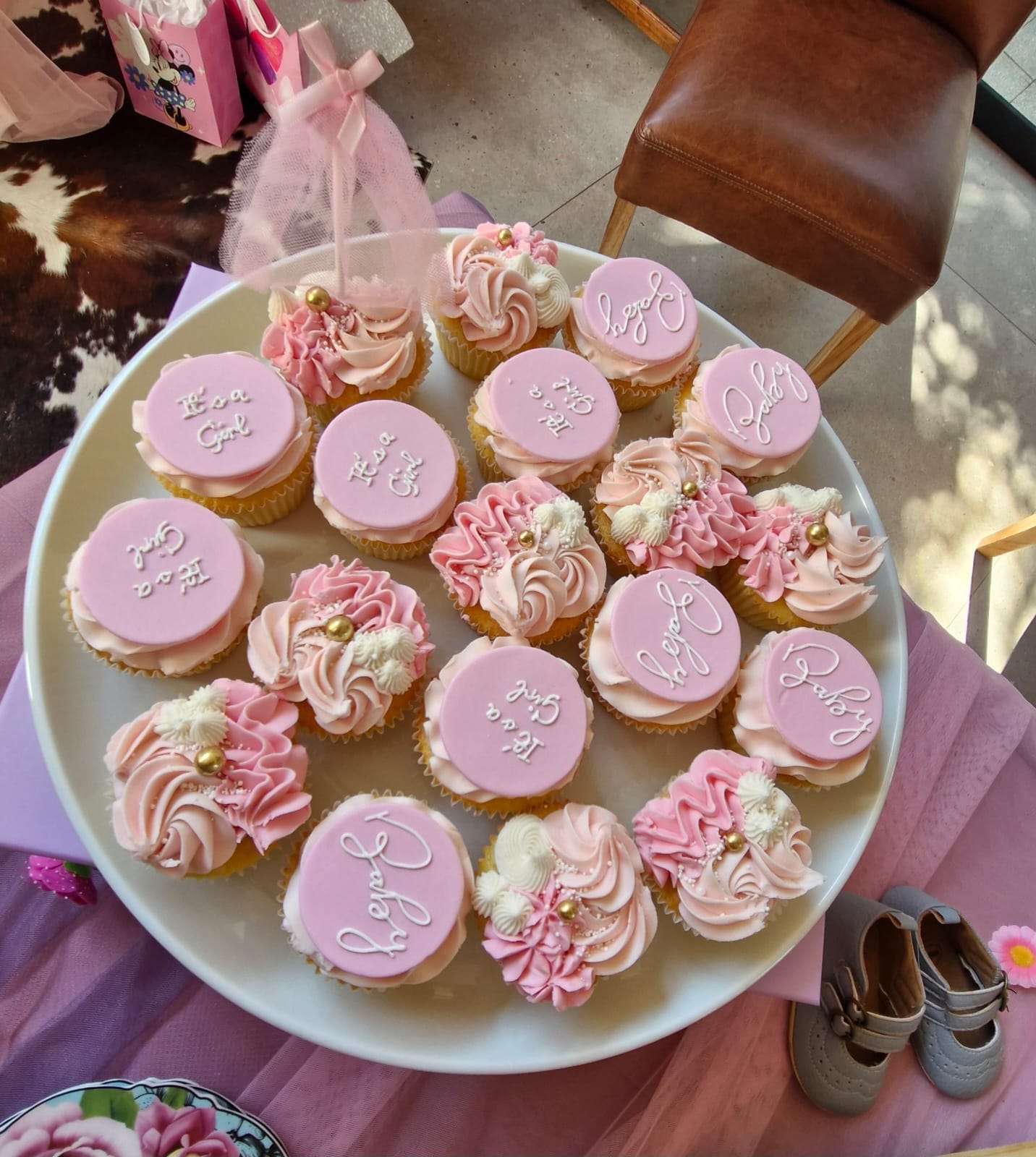 Platter of pink baby shower cupcakes topped with It's a Girl and Baby fondant discs